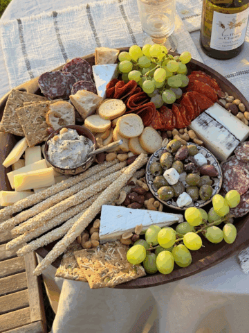 Cheese and charcuterie board with grapes, nuts, and crackers for outdoor dining.