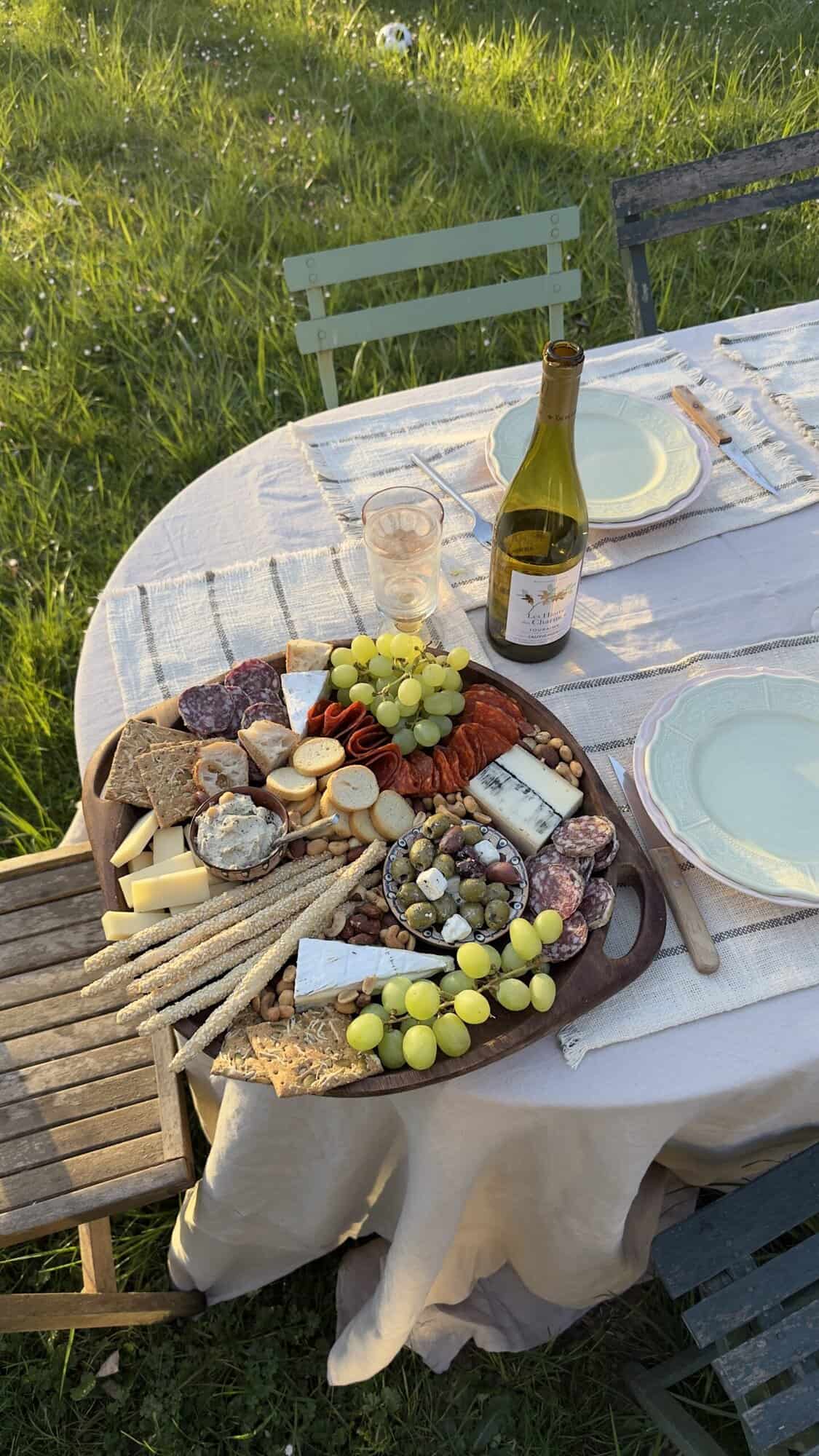 Cheese and charcuterie board with grapes, nuts, and crackers for outdoor dining.