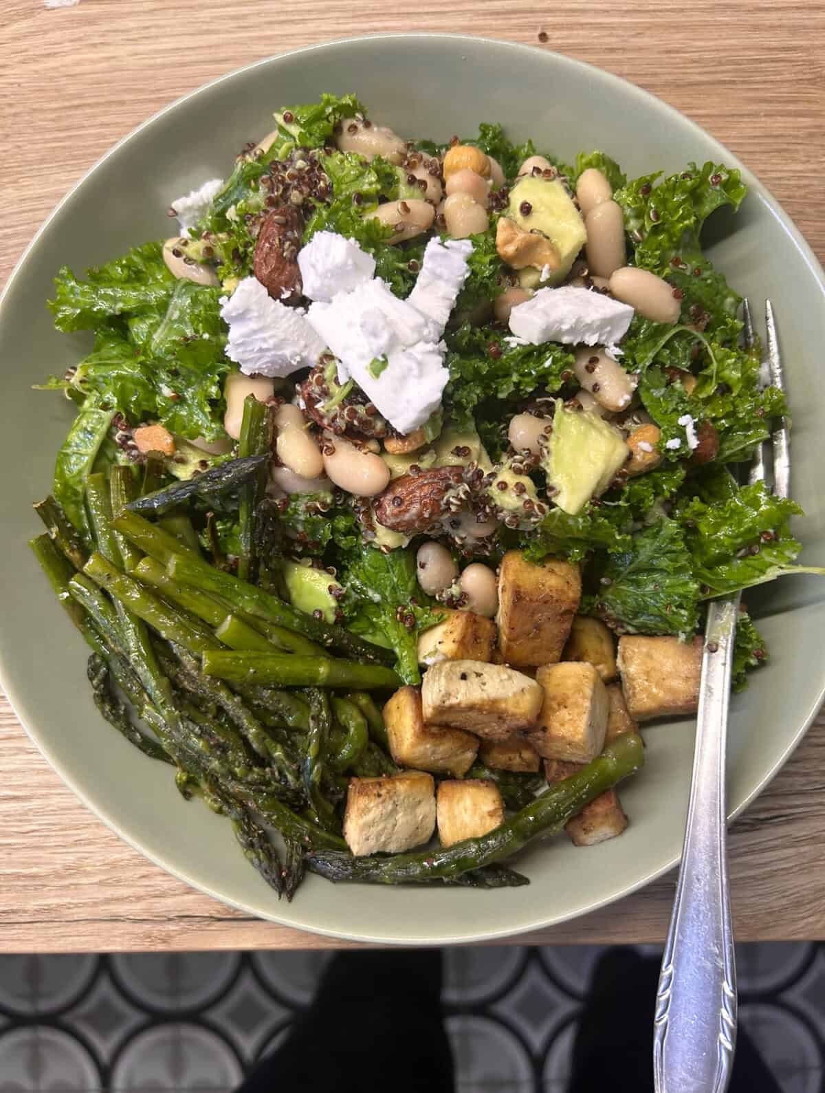 A salad bowl with greens, quinoa, beans, tofu and asparagus, topped with feta cheese.
