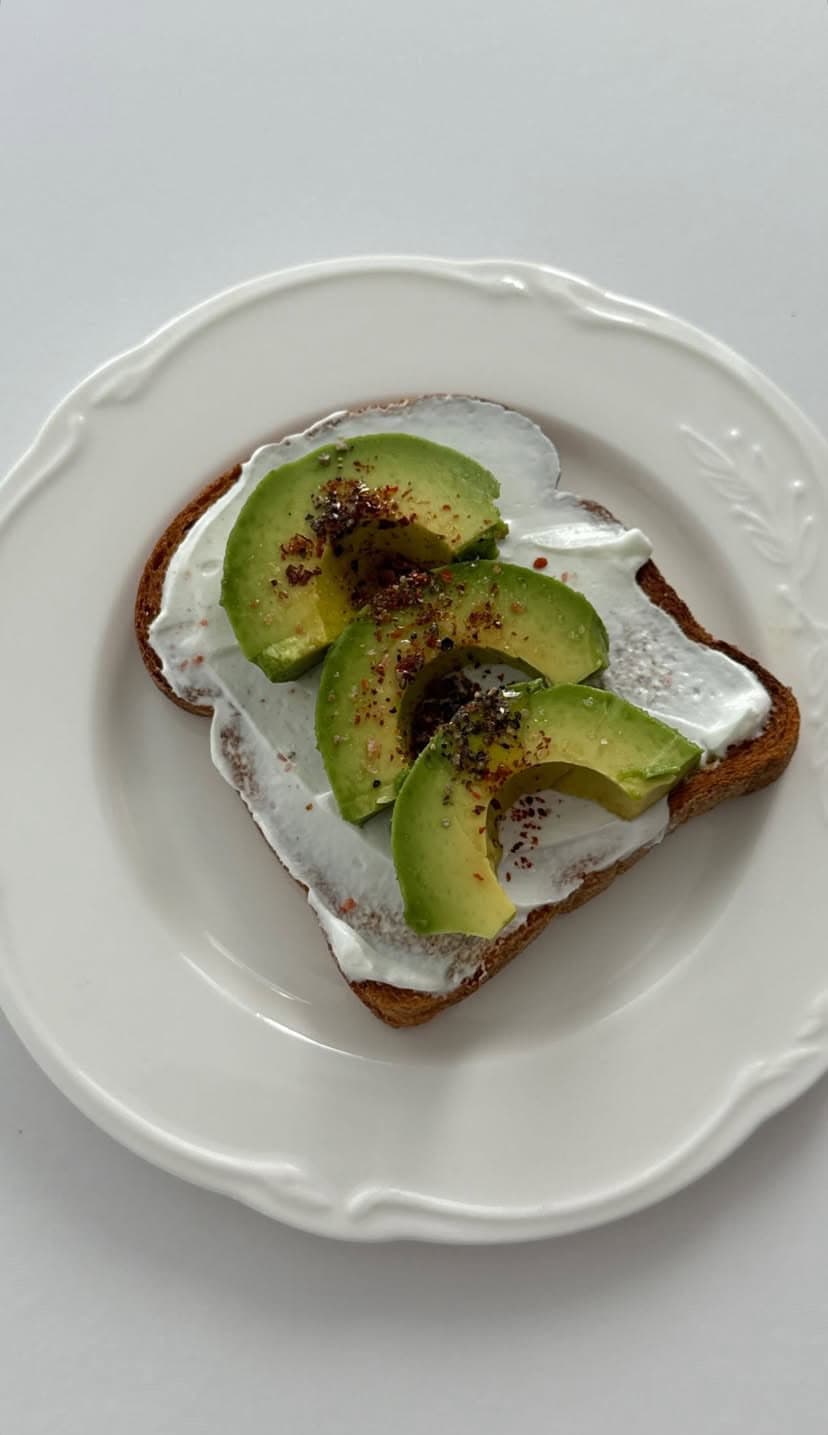 Fresh avocado toast with creamy yogurt spread on whole grain bread, topped with cracked black pepper and sumac.