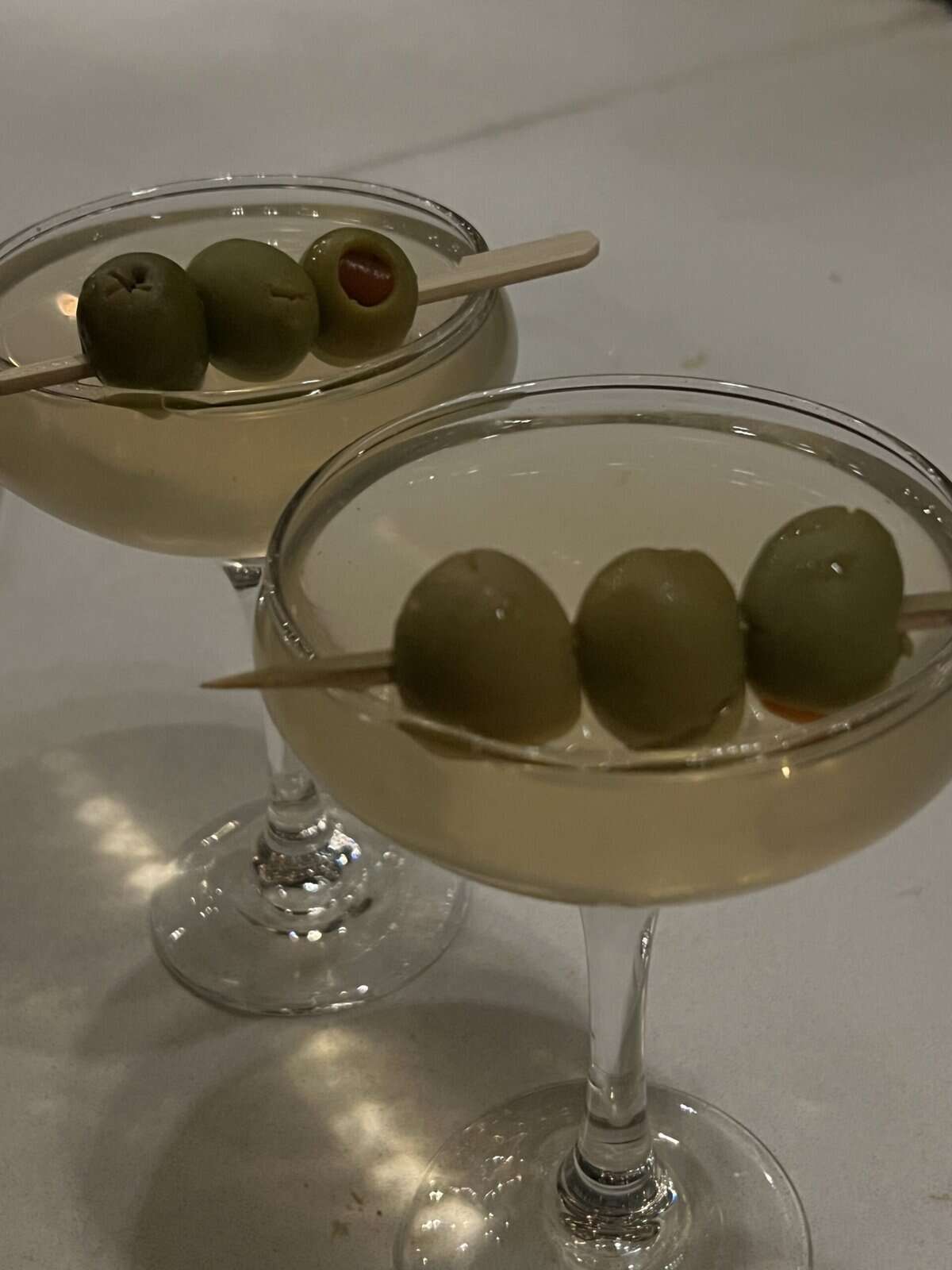 Olive martini cocktails in coupe glasses with green olives on skewers.