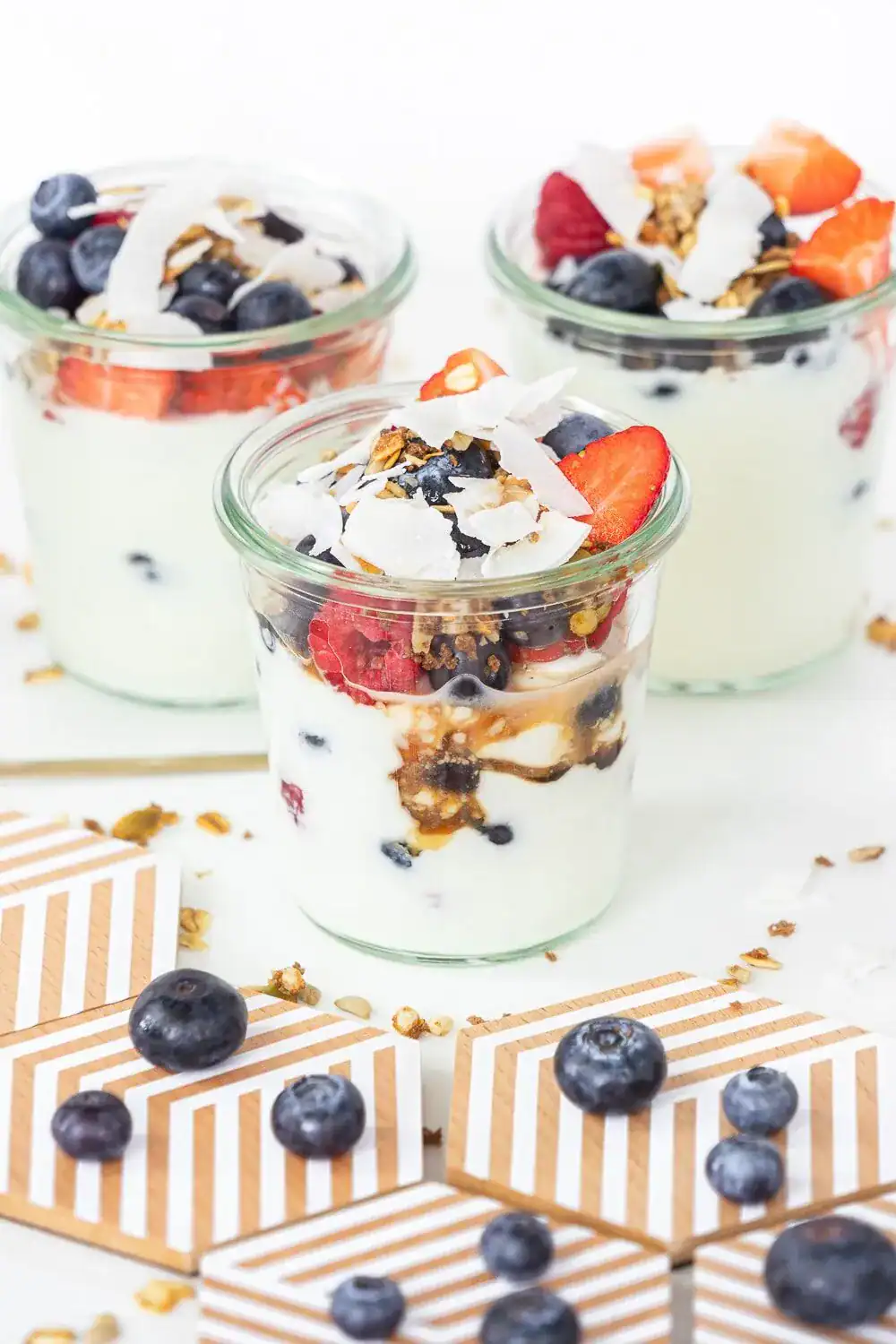 Fresh blueberry and strawberry yogurt parfaits with granola and coconut flakes in glass jars.
