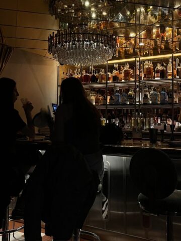 Two girls sitting an opulent bar with a chandelier overhead.