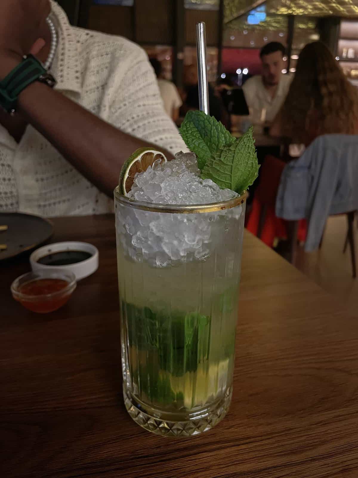 A mojito in a tall glass on the table at a restaurant.