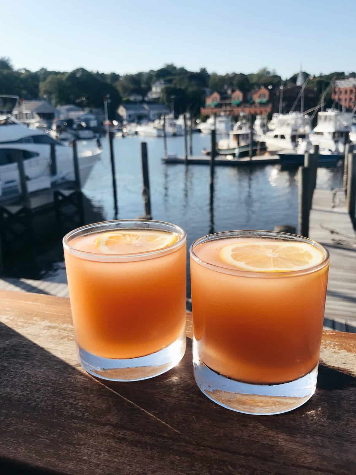 Two Seabreeze cocktails sitting on a wooden balcony overlooking the sea.