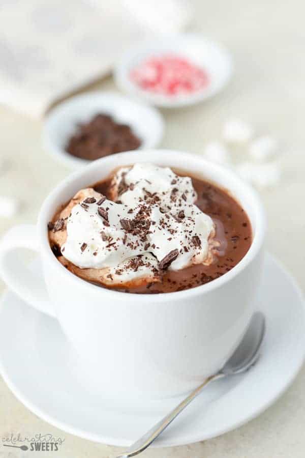 A close up of homemade hot cocoa in a white mug, topped with whipped cream and chocolate shavings.