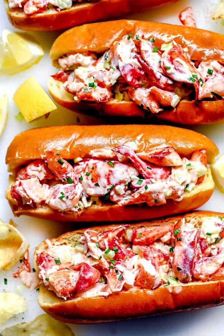 Lobster rolls with fresh lobster meat, chopped chives, and a creamy dressing in toasted buns, served with lemon wedges on a white plate, highlighting seafood and summer lunch ideas from Simply Fresh Foodie.