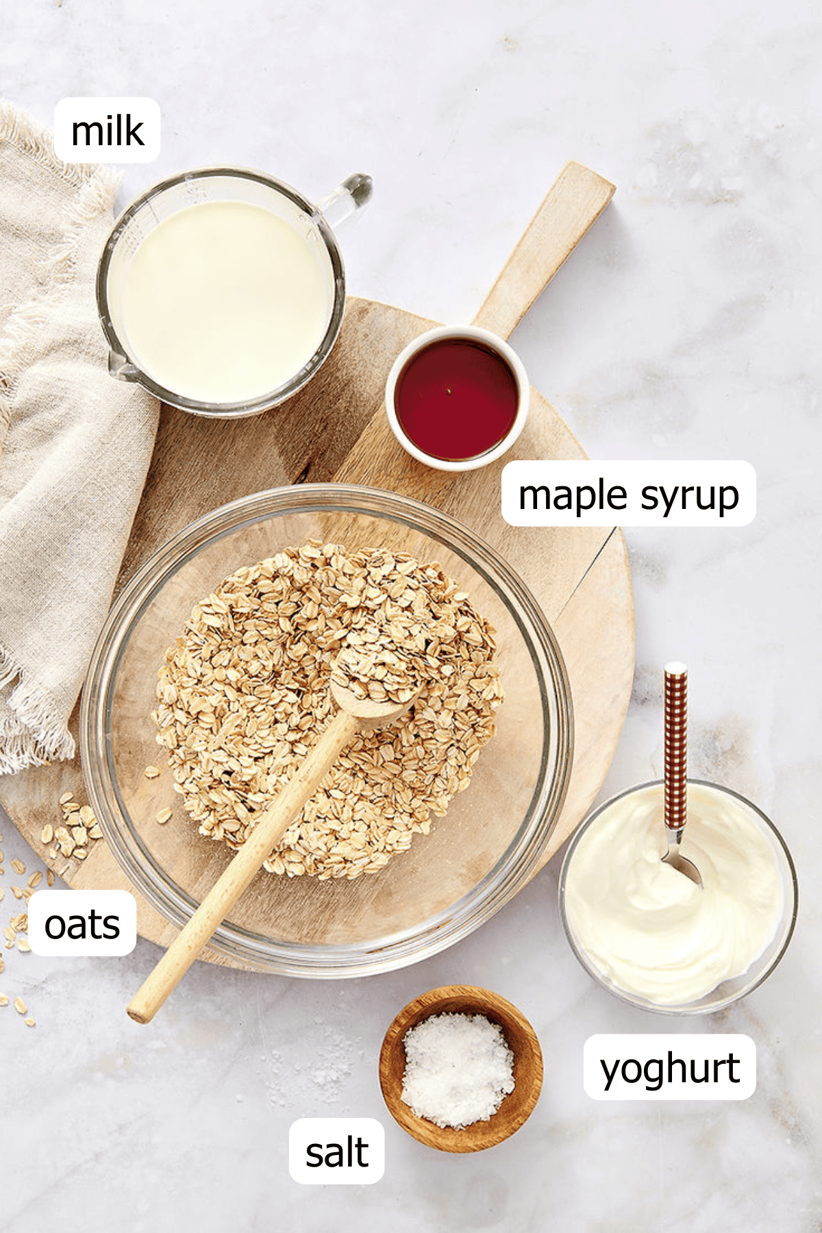 Overhead shot of overnight oats ingredients with text overlay picturing: milk, maple syrup, oats, salt and yoghurt.