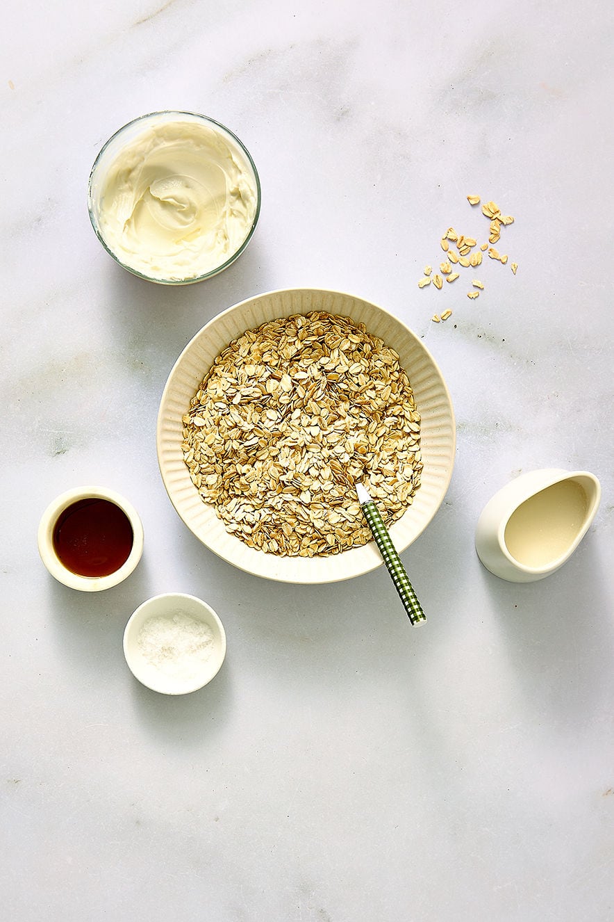 Overhead view of overnight oats ingredients including old-fashioned rolled oats in a large bowl, coconut milk, yoghurt, salt and maple syrup.