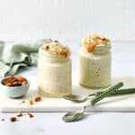 Creamy overnight oats with coconut milk topped with peanut butter and chopped almonds, served in glass jars with fresh almonds on a white marble slab. Perfect for healthy meal prep or breakfast ideas.