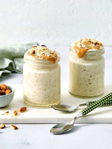 Creamy overnight oats with coconut milk topped with peanut butter and chopped almonds, served in glass jars with fresh almonds on a white marble slab. Perfect for healthy meal prep or breakfast ideas.