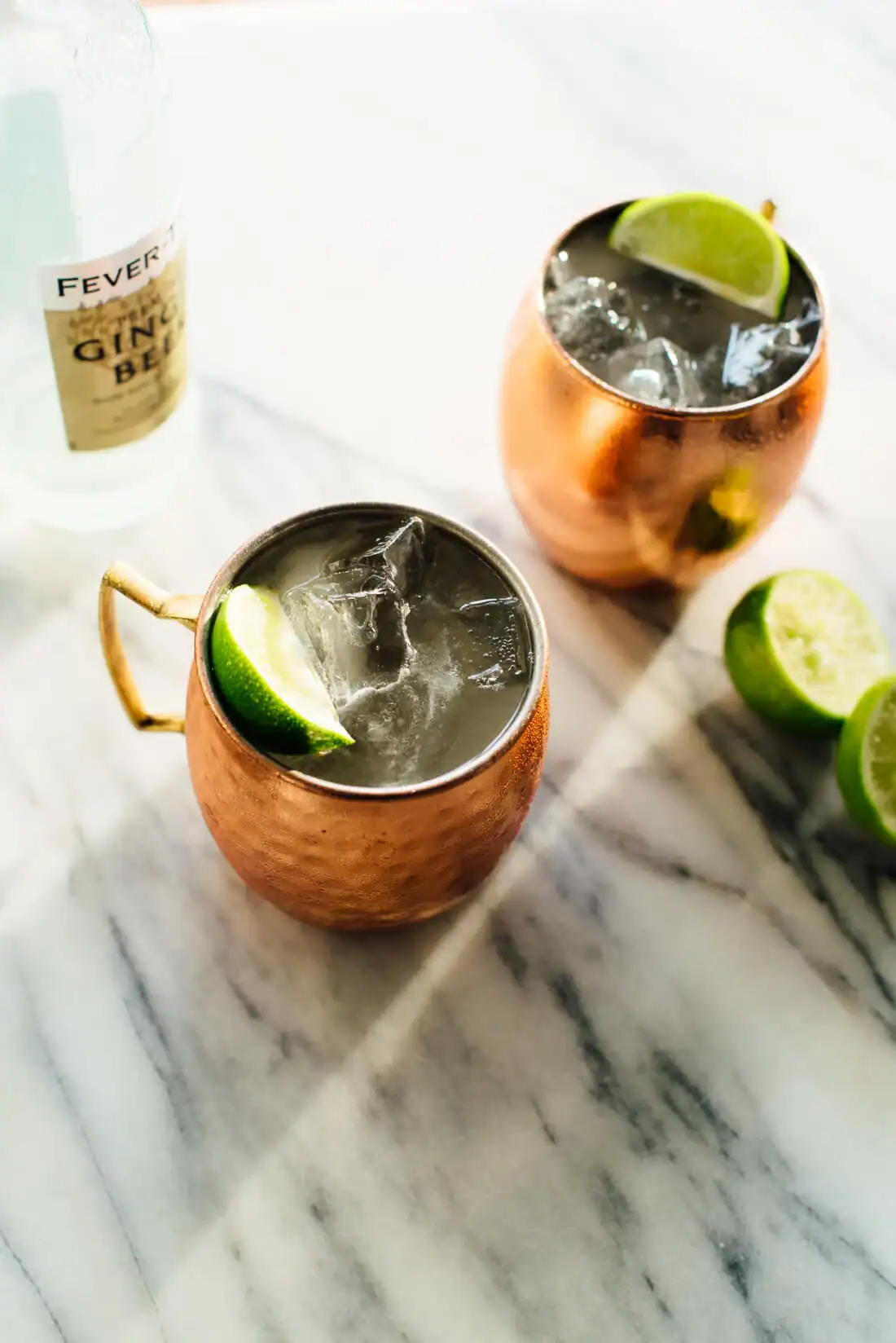 Two Moscow Mules served in copper mugs and topped with lime wedges.