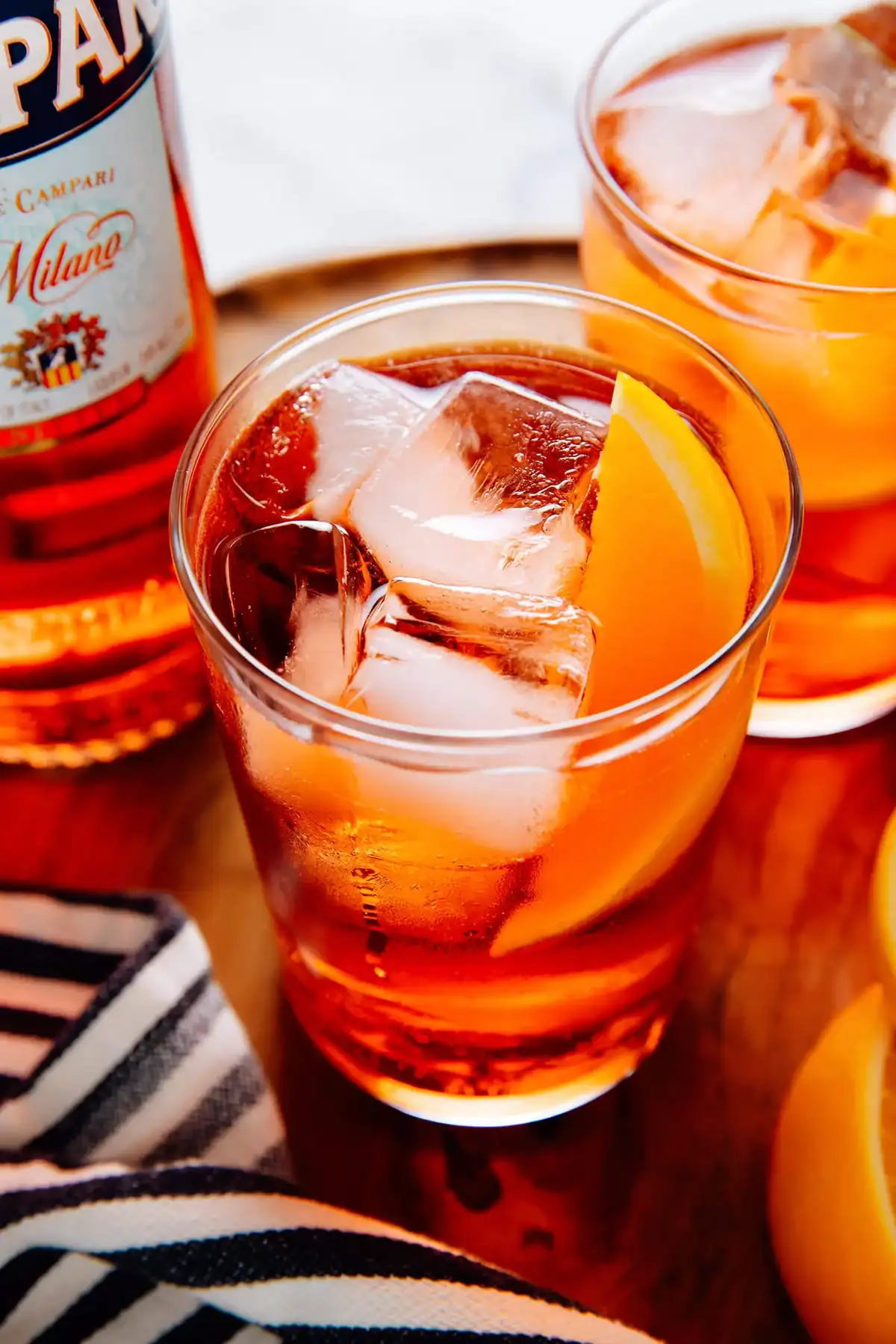 An Americano cocktail in a glass with ice and an orange slice.
