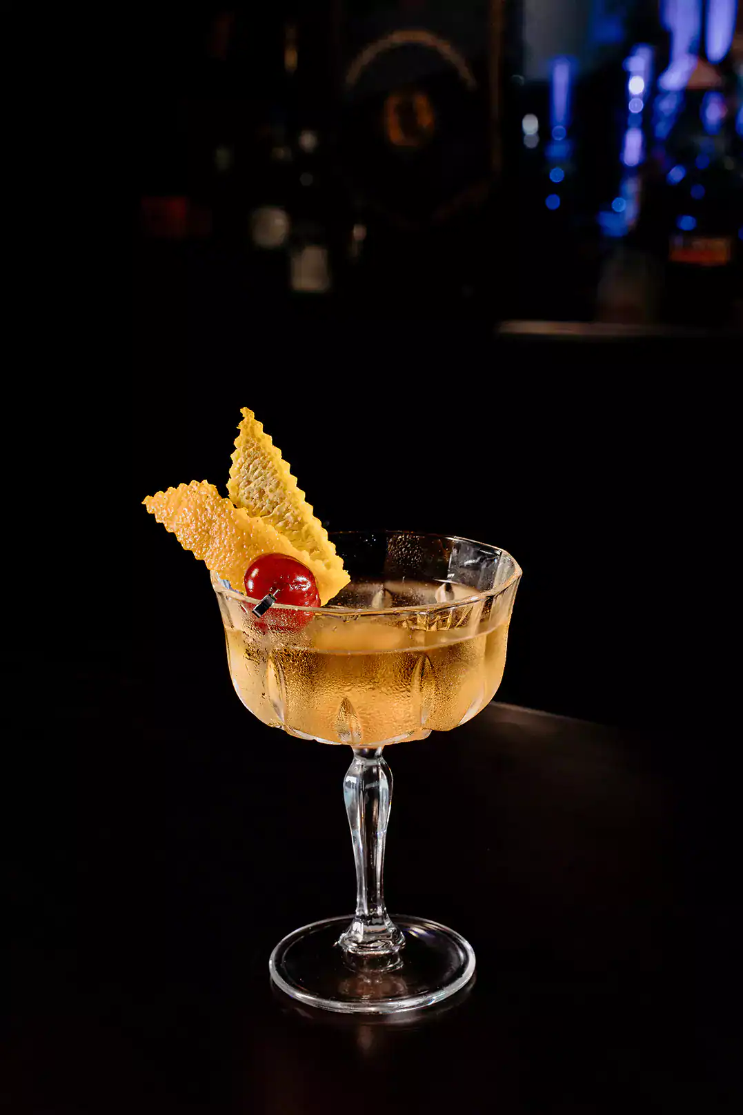 A champagne cocktail in a copue glass, garnished with a cherry and citrus peel.