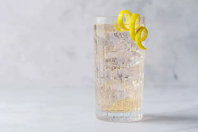 An elderflower cocktail in a highball glass with ice and a lemon peel garnish.