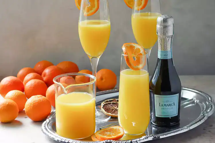 Mimosas on a silver tray with LaMarca prosecco and oranges in the background.