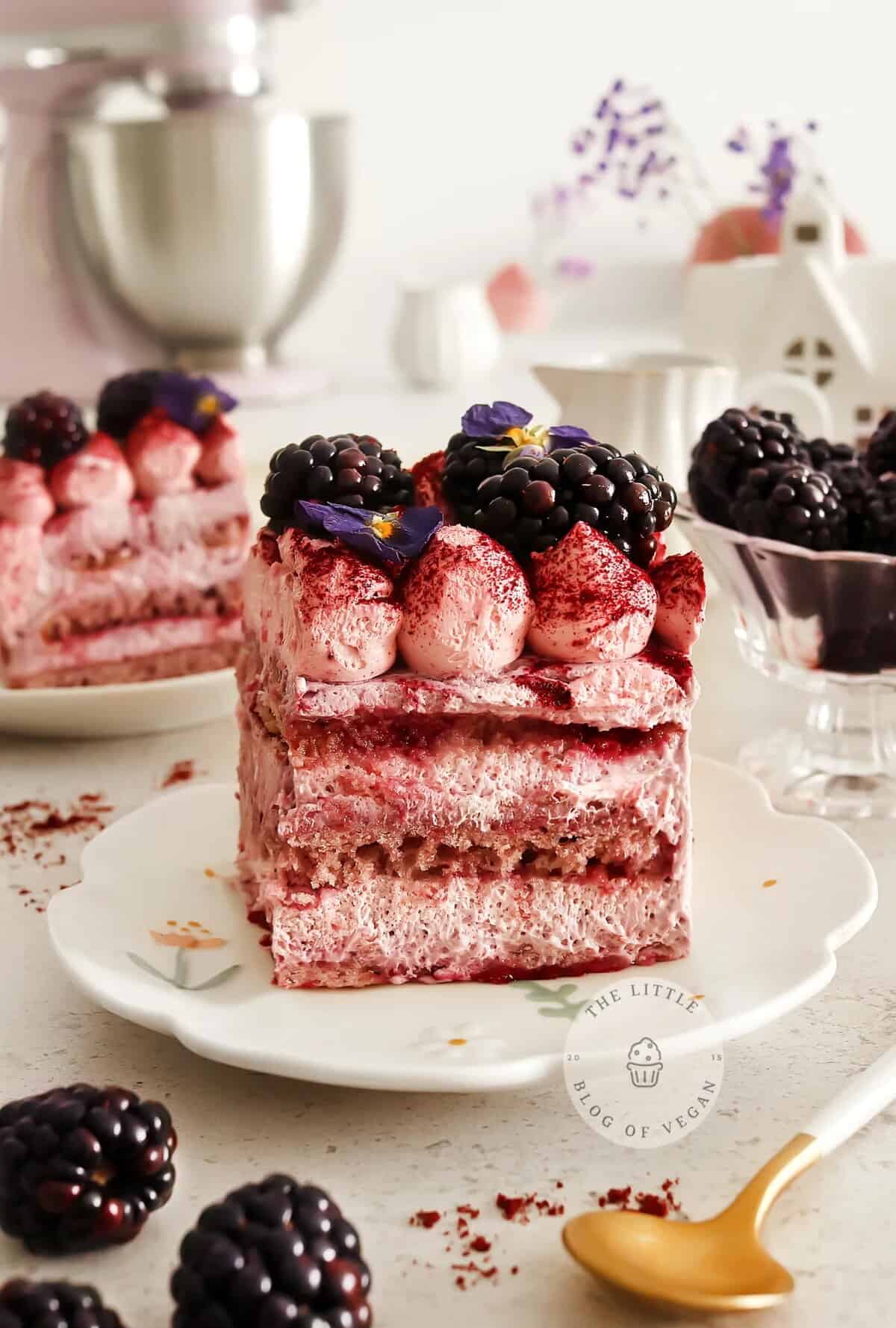 A tall serving of tiramisu with rich red colouring and white cream filling, topped with fresh blackberries and edible violets.