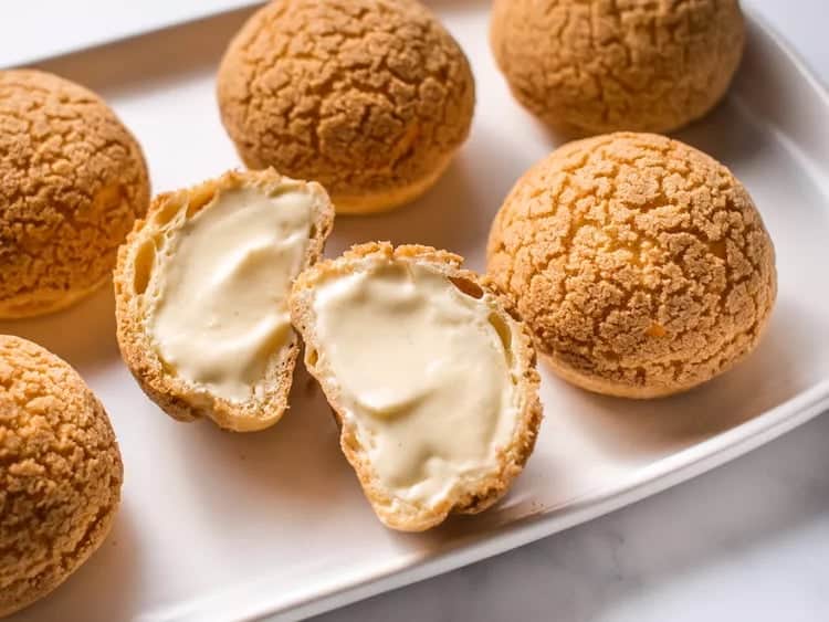 Choux pastry balls with crackling surfaces, with one sliced down the middle to showcase a rich, creamy filling.