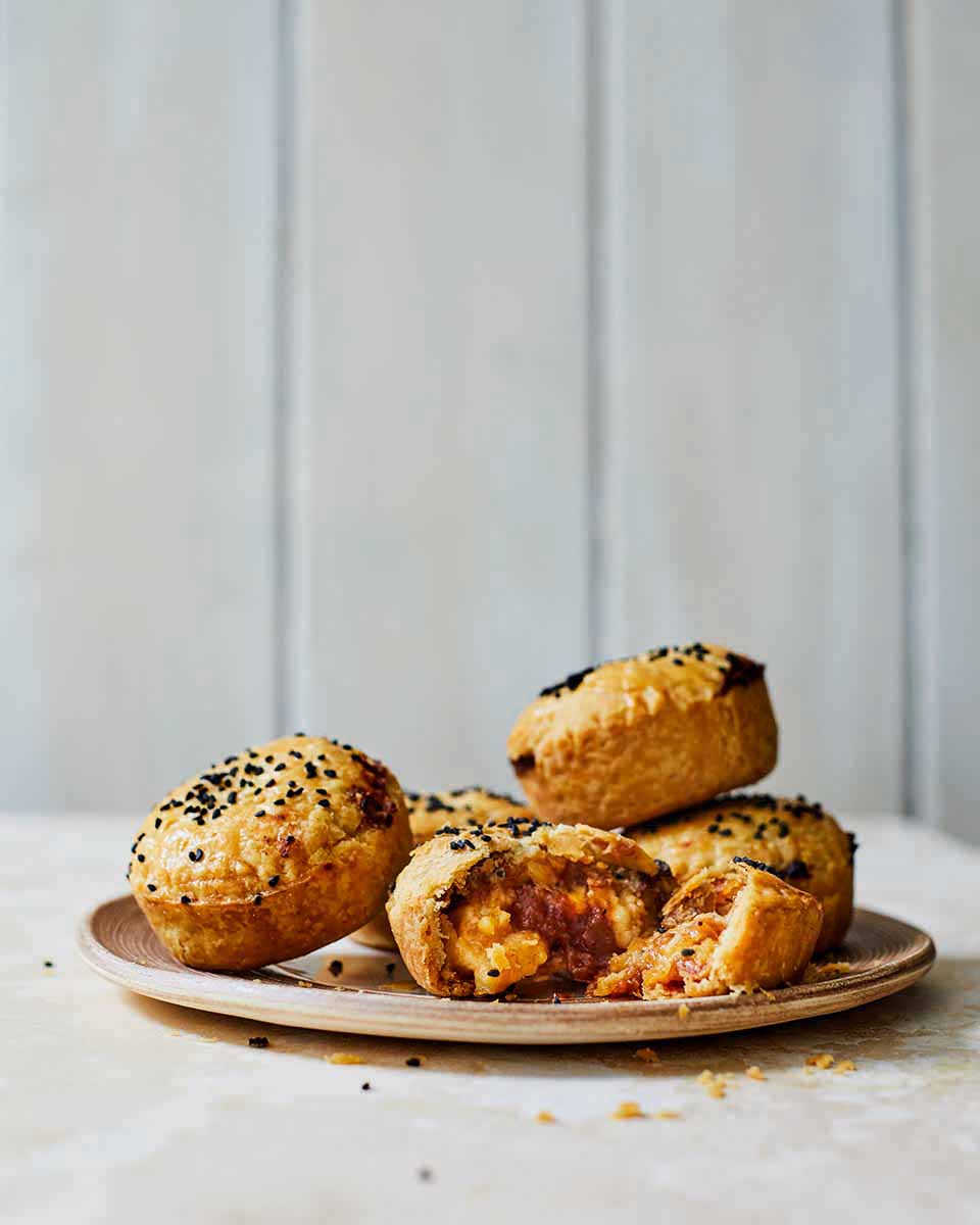 Brown savoury pastries with black sesame seeds on top, served on a rustic plate, showcasing a flaky, crispy exterior and a delicious chutney and cheese filling.