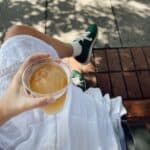 Thumbnail image for article about the best non-alcoholic beers in Australia showing a person holding a glass of a cold beverage while sitting outdoors on a sunny day.