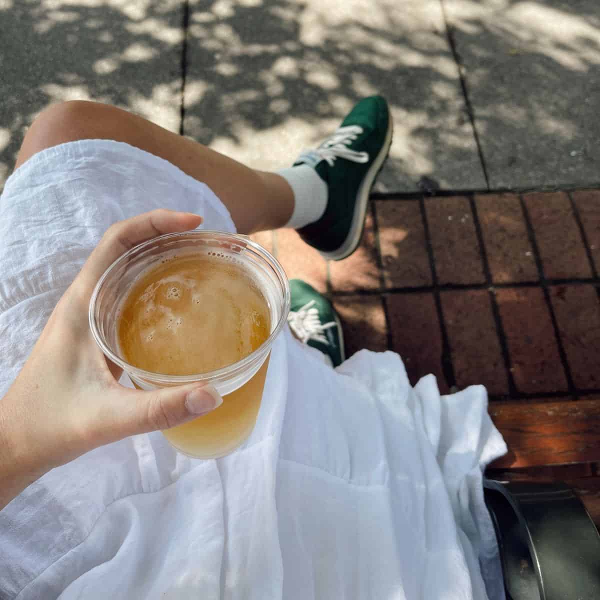 Thumbnail image for article about the best non-alcoholic beers in Australia showing a person holding a glass of a cold beverage while sitting outdoors on a sunny day.
