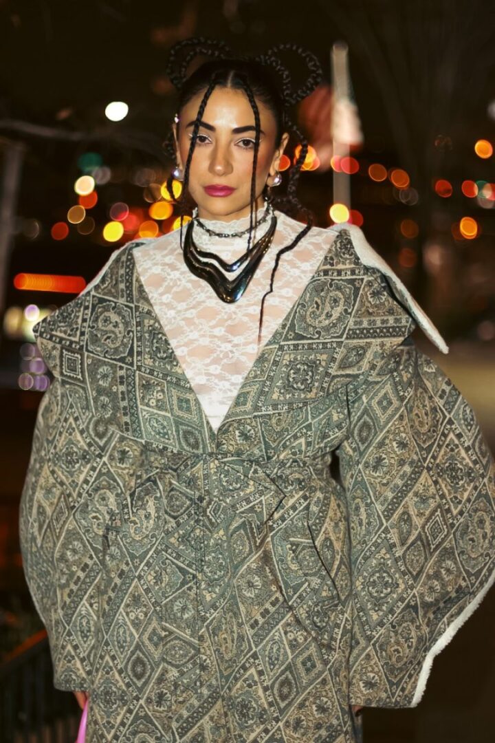 Model in ornate patterned kimono-style coat with space buns and layered necklaces at NYFW