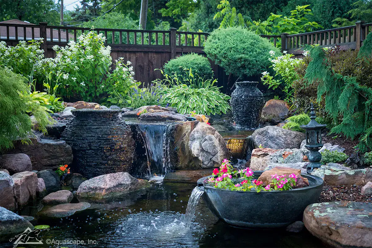 Lush backyard pond with water features, rocks, and vibrant flowers for serene outdoor landscaping.