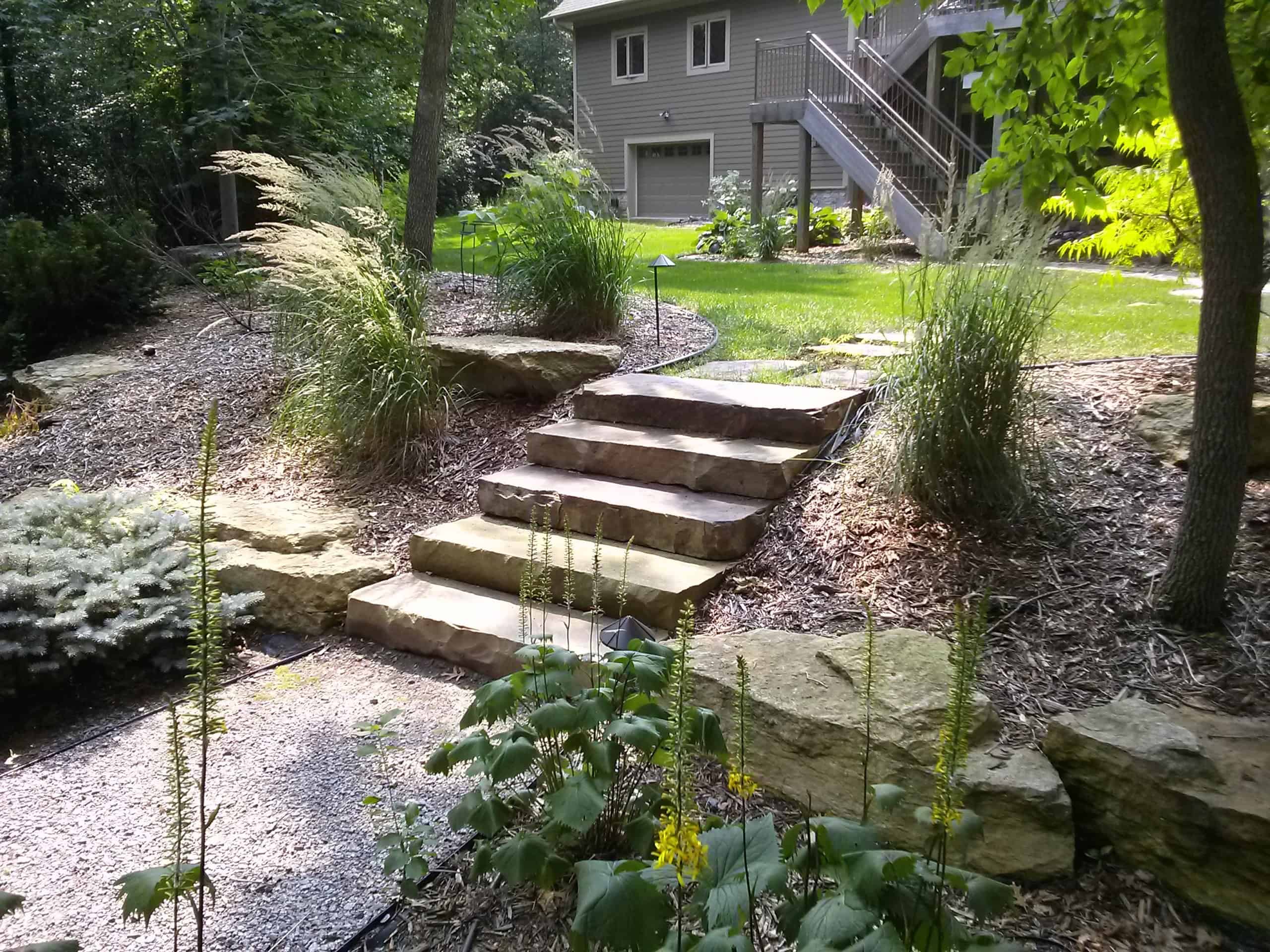 Natural stone staircase in a landscaped garden with lush greenery and mature trees, enhancing outdoor curb appeal.