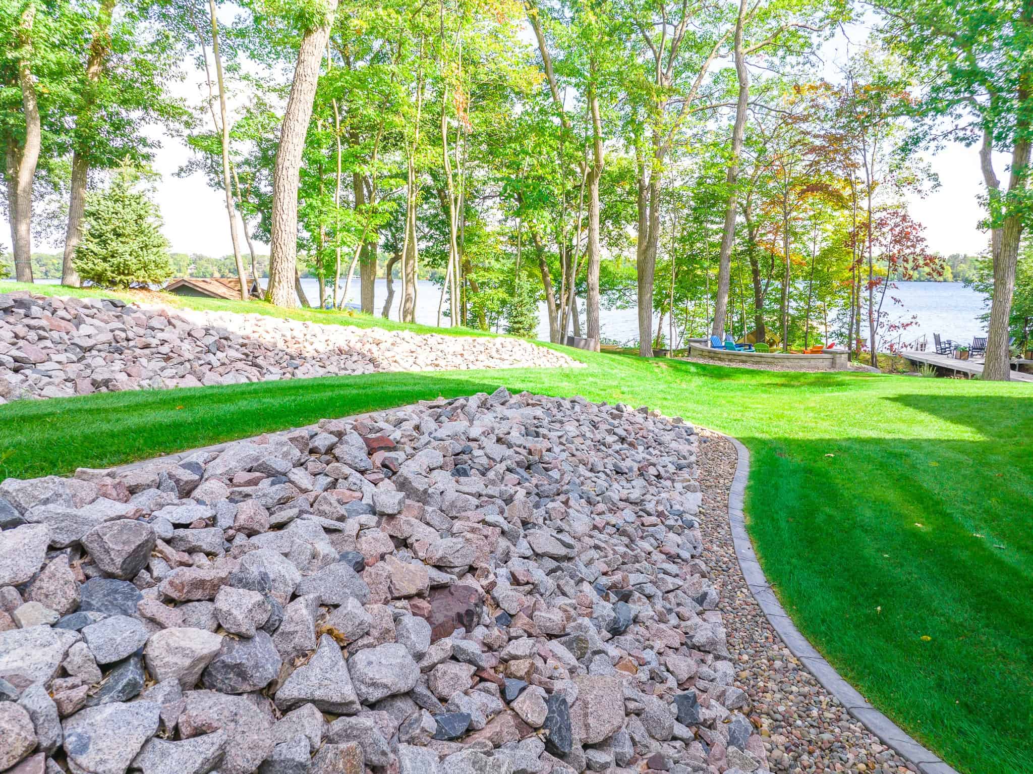 Lush green lawn with decorative rocks and trees near a lake, showcasing professional landscaping by Supreme Lawn.
