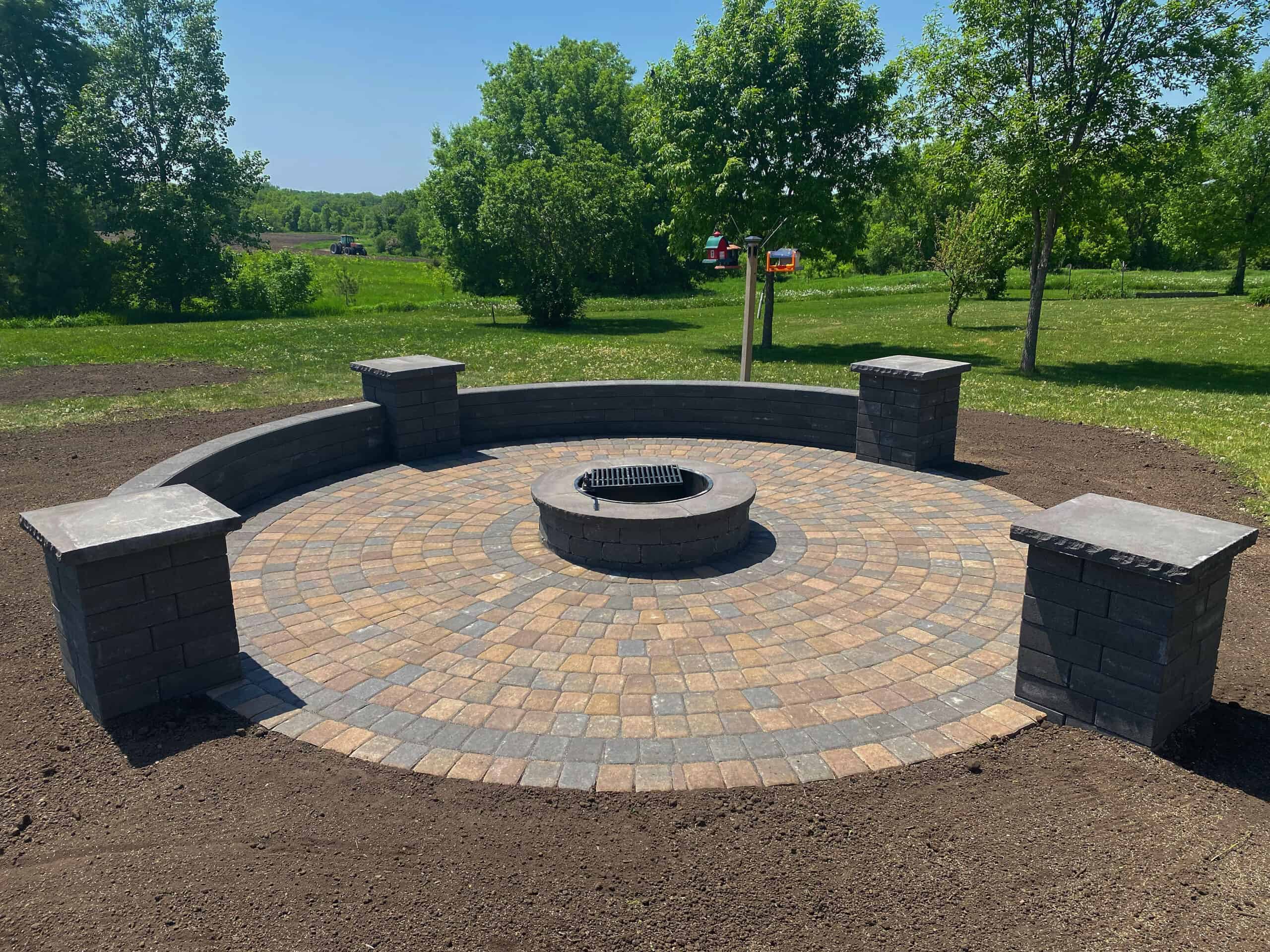 Elegant outdoor fire pit with brick seating area and lush green landscape.