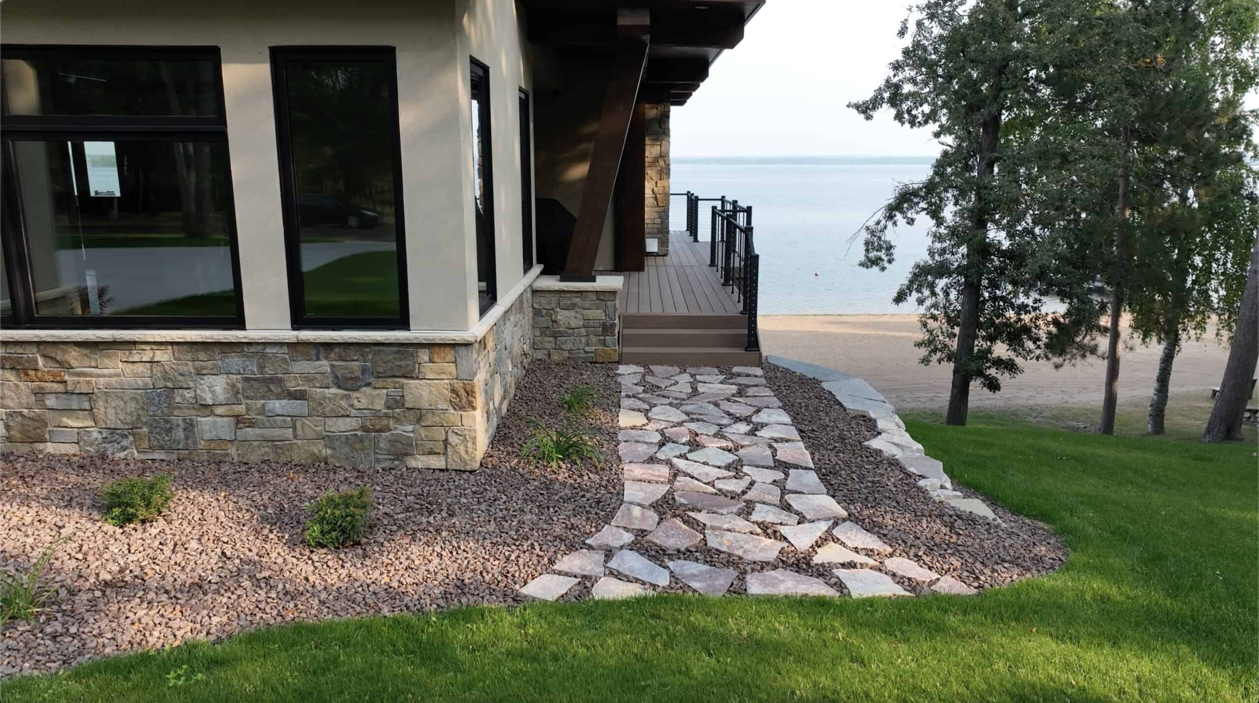Natural stone pathway leading to a lakeside home with landscaped garden and well-maintained grass.