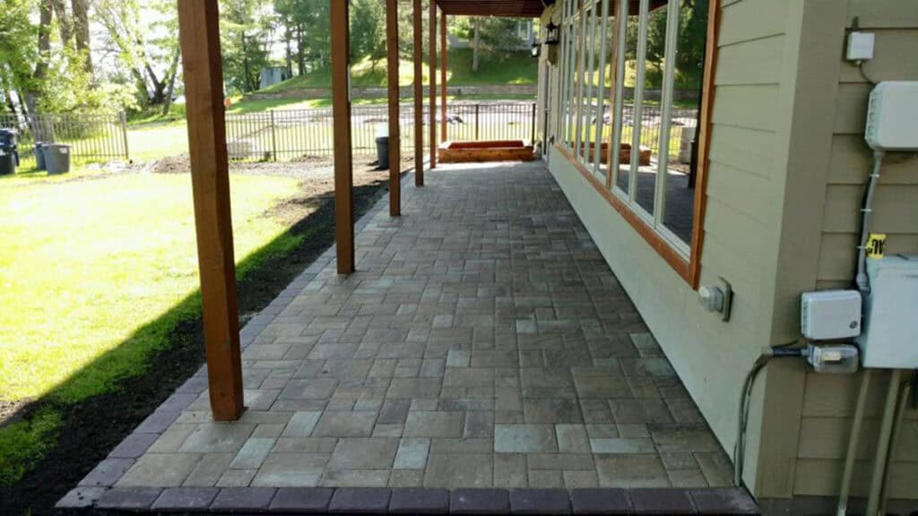 Paver patio with covered porch and surrounding lawn in backyard for outdoor living.