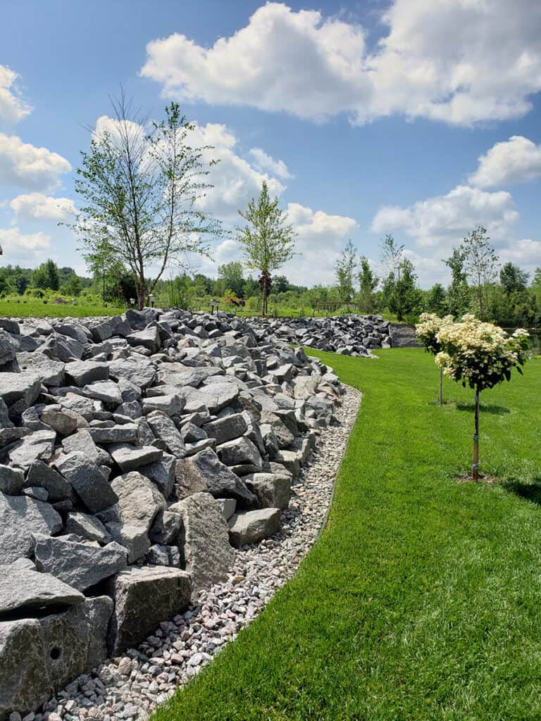 Rocks and gravel landscape border with lush green lawn and young trees in a well-maintained outdoor space.