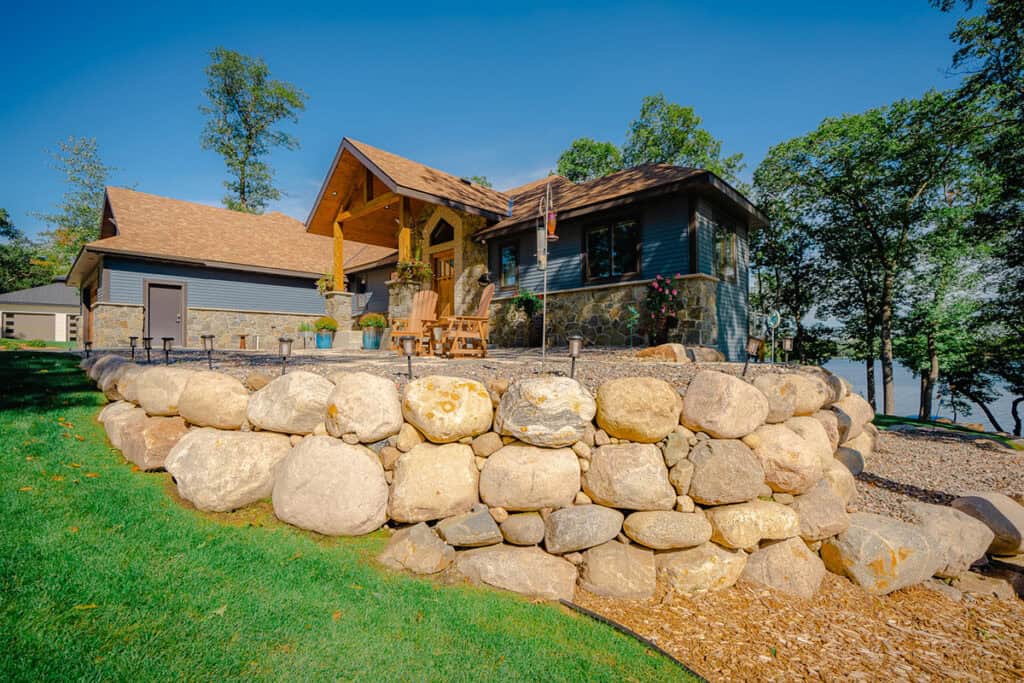 Lush green lawn and landscaped yard with stone retaining wall around a beautiful house.