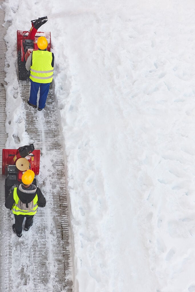 Snow removal with industrial snow blowers on a sidewalk for winter yard maintenance.