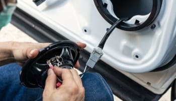 Technician installing car audio system inside vehicle door for enhanced sound quality.