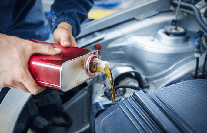 Mechanic pouring oil into a car engine during maintenance at Tatlow Tire.