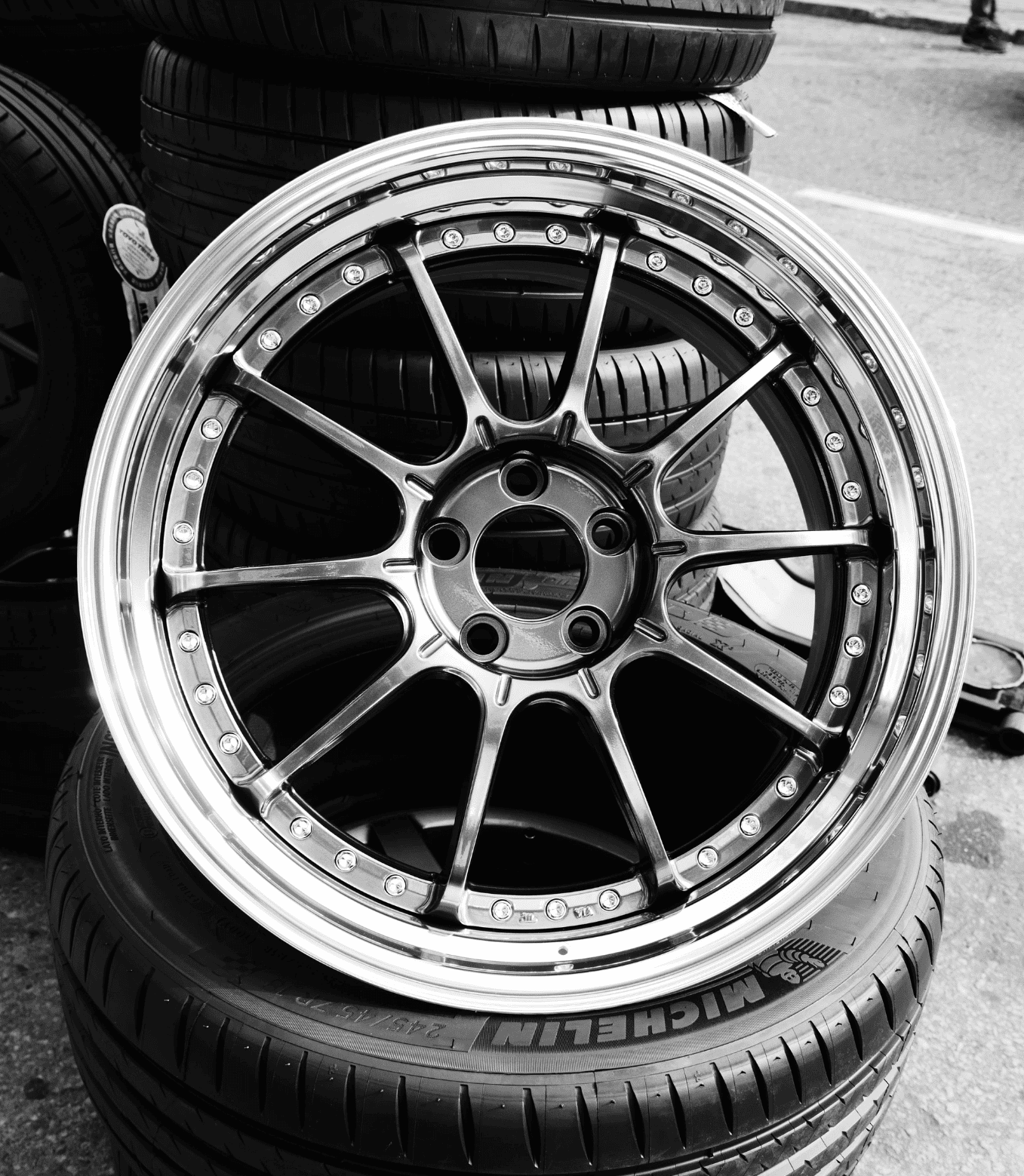 Close-up of black alloy car wheel rim with tires stacked in background.