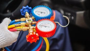 Technician testing A/C system pressure with gauges in vehicle.