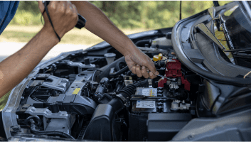 Technician repairing car battery in engine bay at Teays Valley Auto.