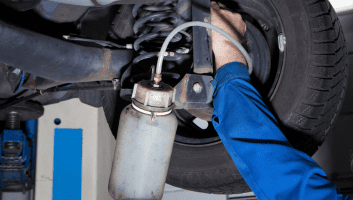 Auto technician performing fluid change on vehicle suspension system.