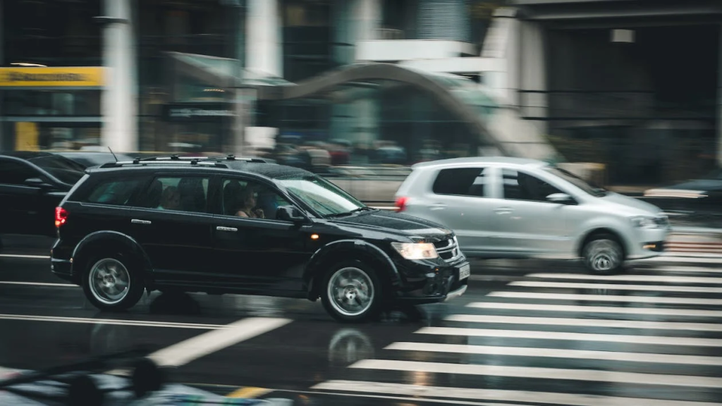 Car crossing pedestrian crosswalk on wet city street during rain.