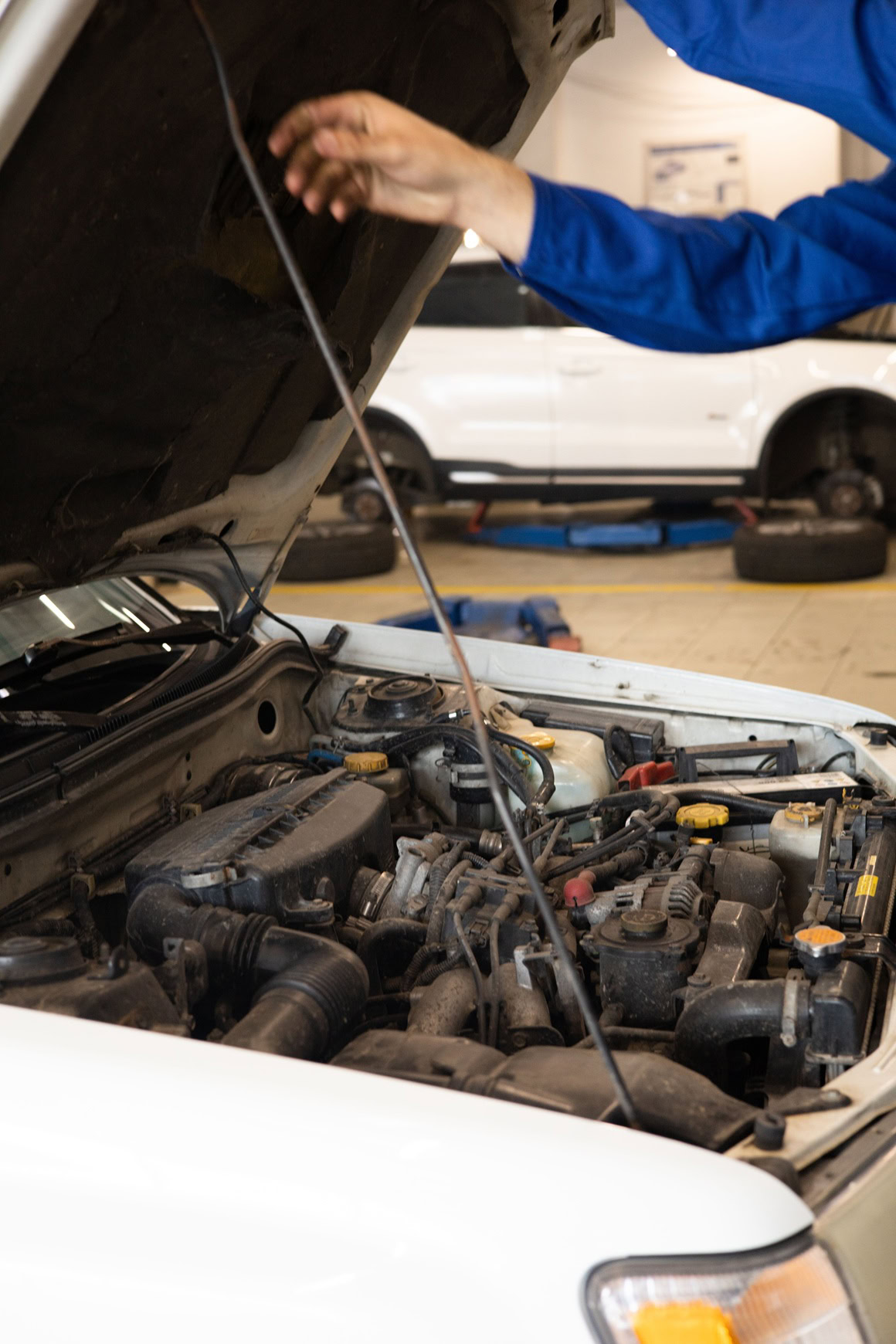 Technician inspecting car engine during tire replacement service.