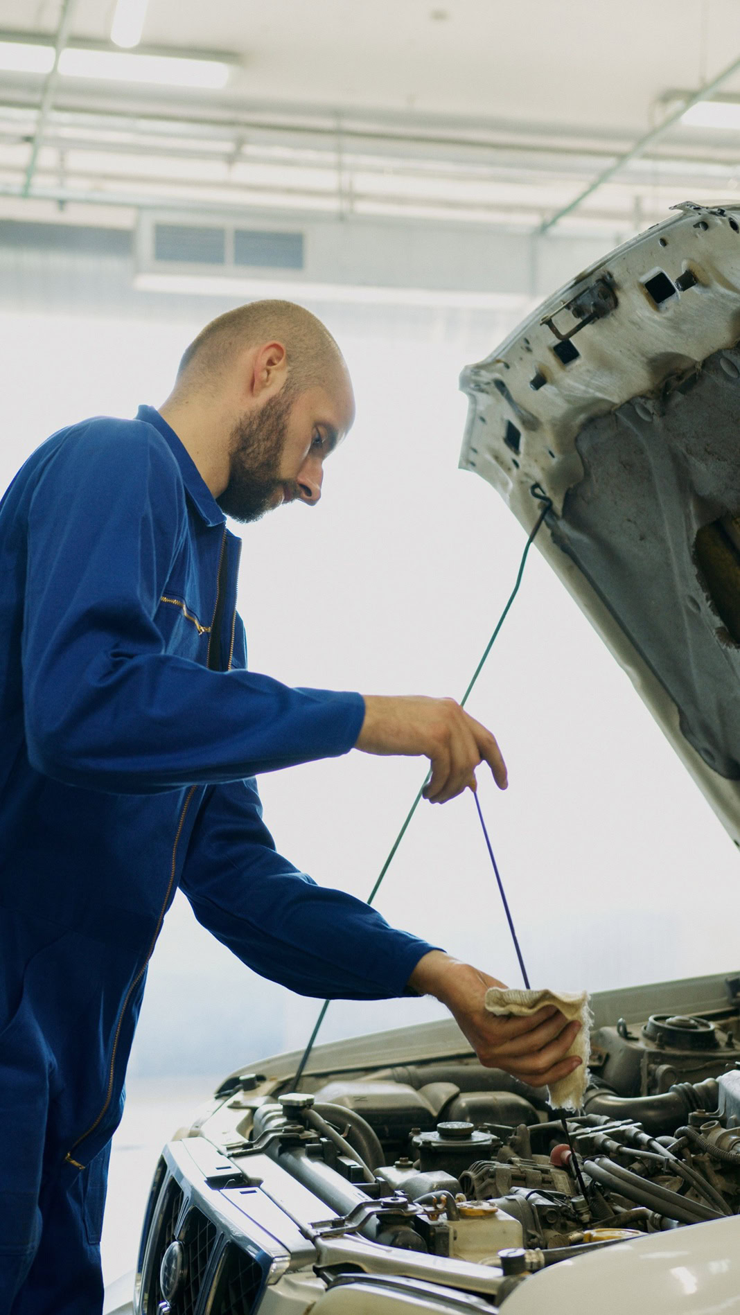 Technician inspecting car engine fluid levels in auto repair shop.
