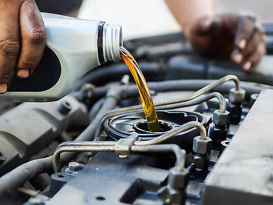Technician pouring engine oil into a car engine during maintenance.
