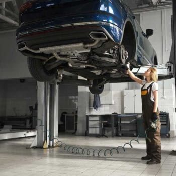 Technician inspecting a car lifted on a hydraulic lift at Techline Motors.