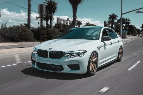 White BMW luxury sedan driving on urban road with palm trees.
