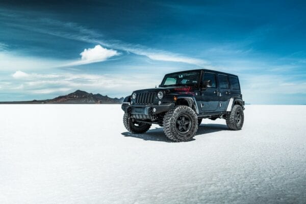 Black Jeep on salt flats with mountains in background.