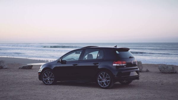 Black Volkswagen Golf parked on the beach at sunset.