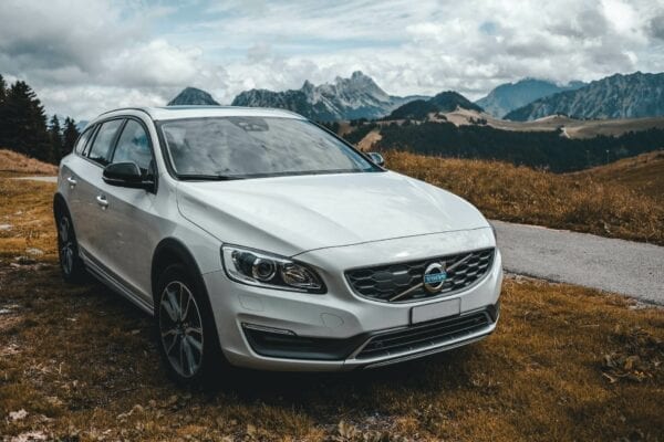 White Volvo station wagon parked on mountain trail with mountains in background.